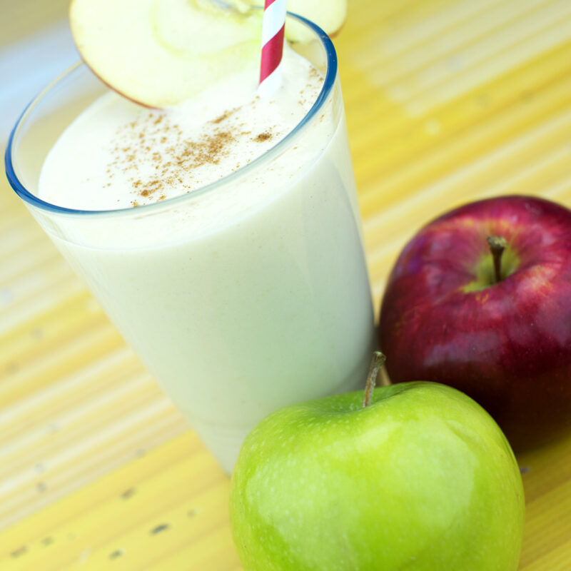 A creamy apple pie smoothie in a glass, topped with a sprinkle of cinnamon and a slice of apple for garnish.