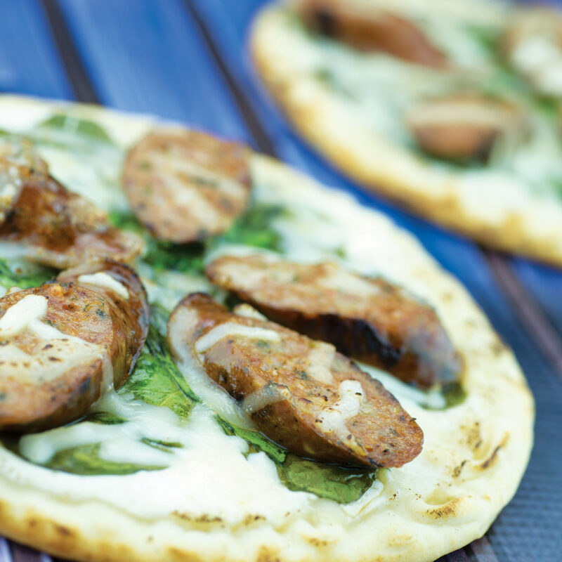 Pita pizza alfredo topped with sausage slices on a plate.