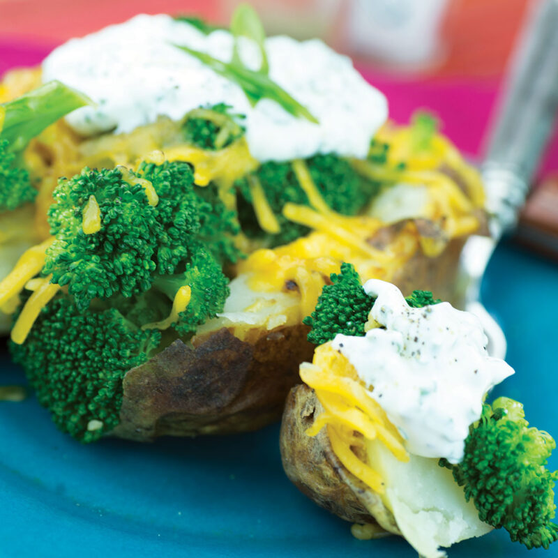 Stuffed baked potato topped with broccoli and melted cheese on a plate.
